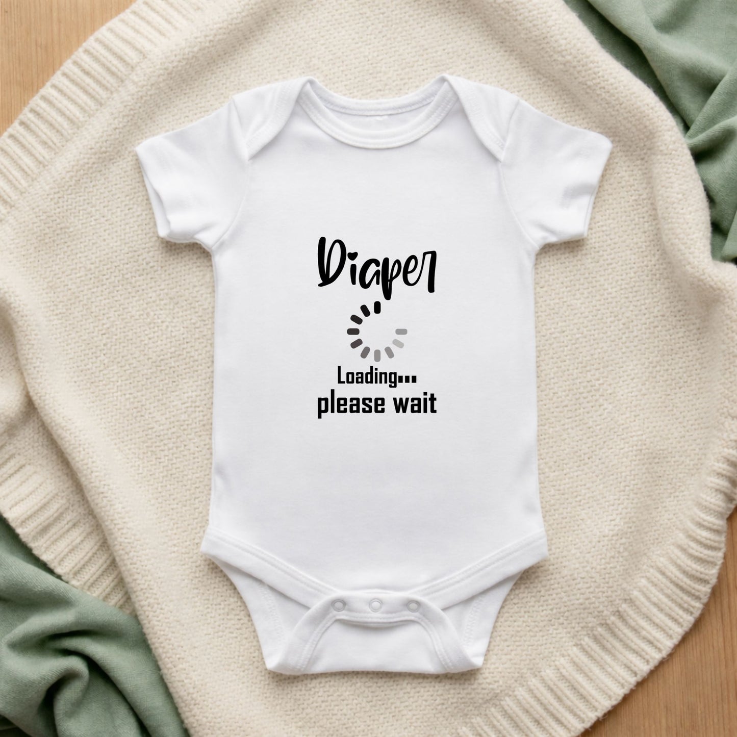 White baby onesie with 'Diaper Loading Please Wait' text on a beige blanket.