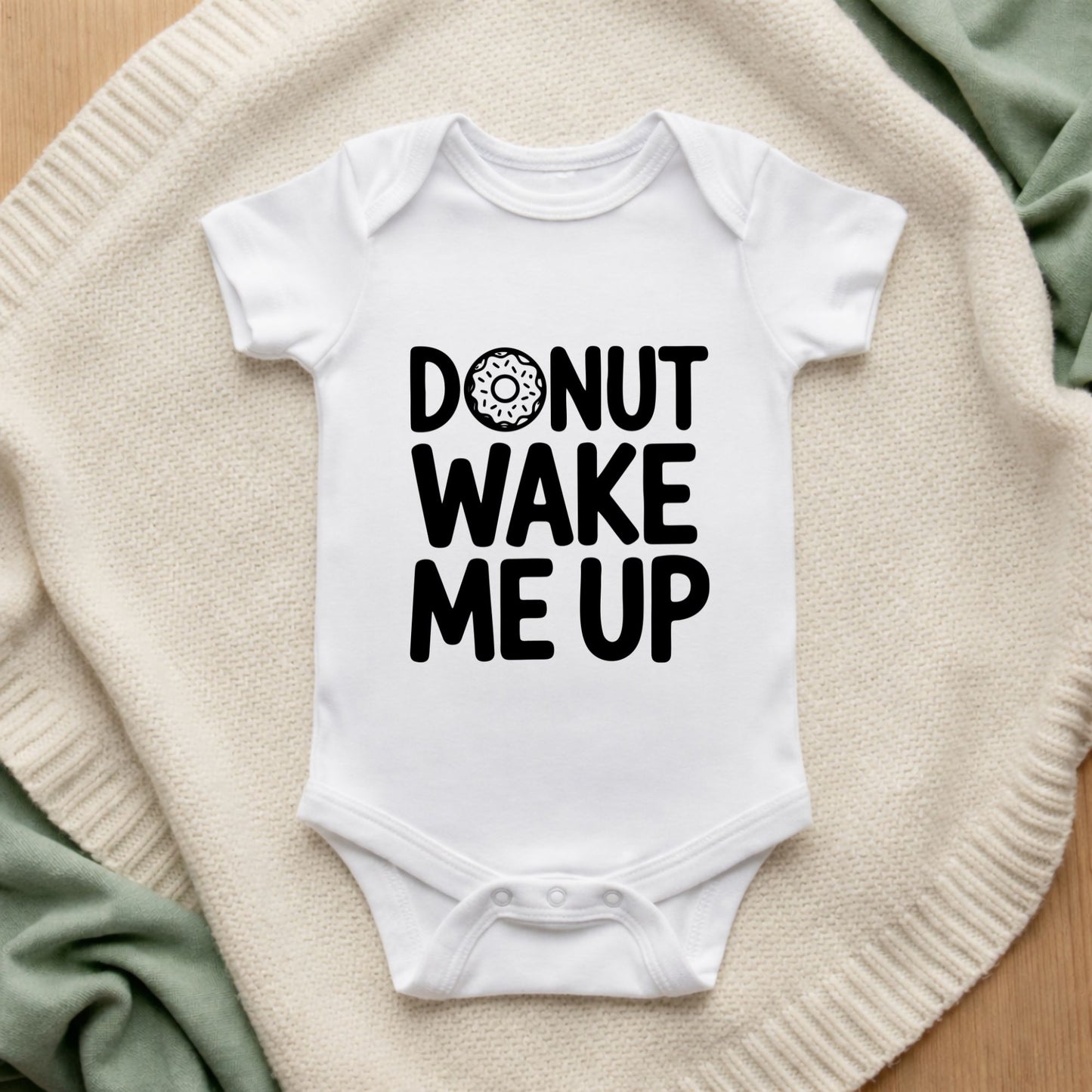 White baby onesie with 'Donut Wake Me Up' text on a textured surface Donut Wake Me Up Baby Bodysuit