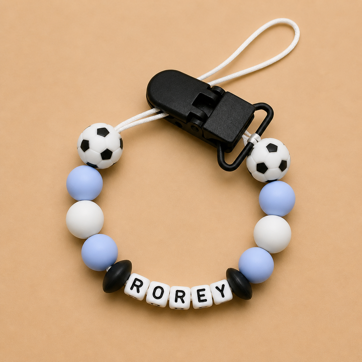 silicone beaded dummy clip with soccer ball and letter beads on a beige background