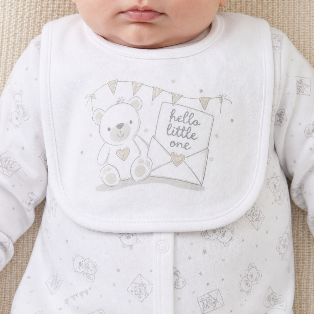 Baby bib with teddy bear design and 'hello little one' text on a textured surface