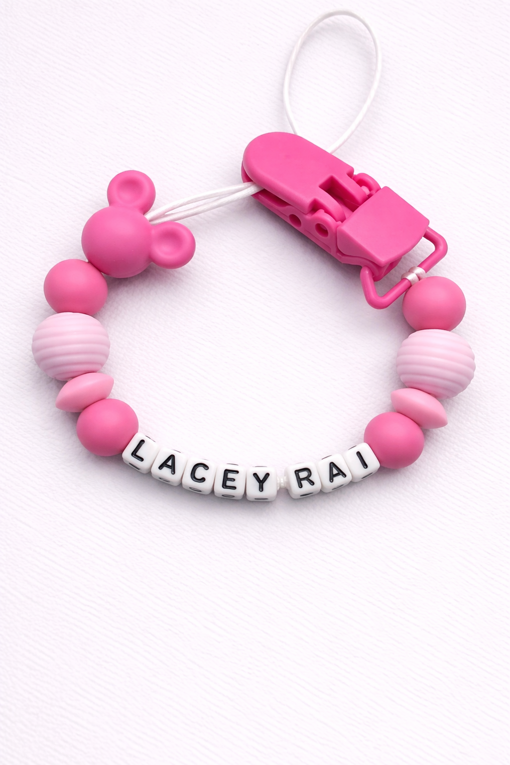 Pink and white dummy clip with 'LACEY RAI' on a white background