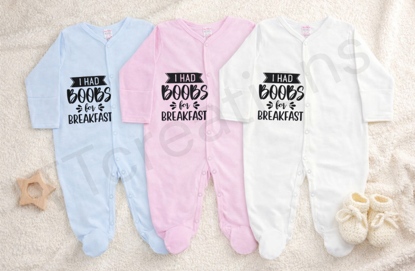 blue, pink, and white baby onesies with the text “I Had Boobs For Breakfast” displayed on a neutral background.