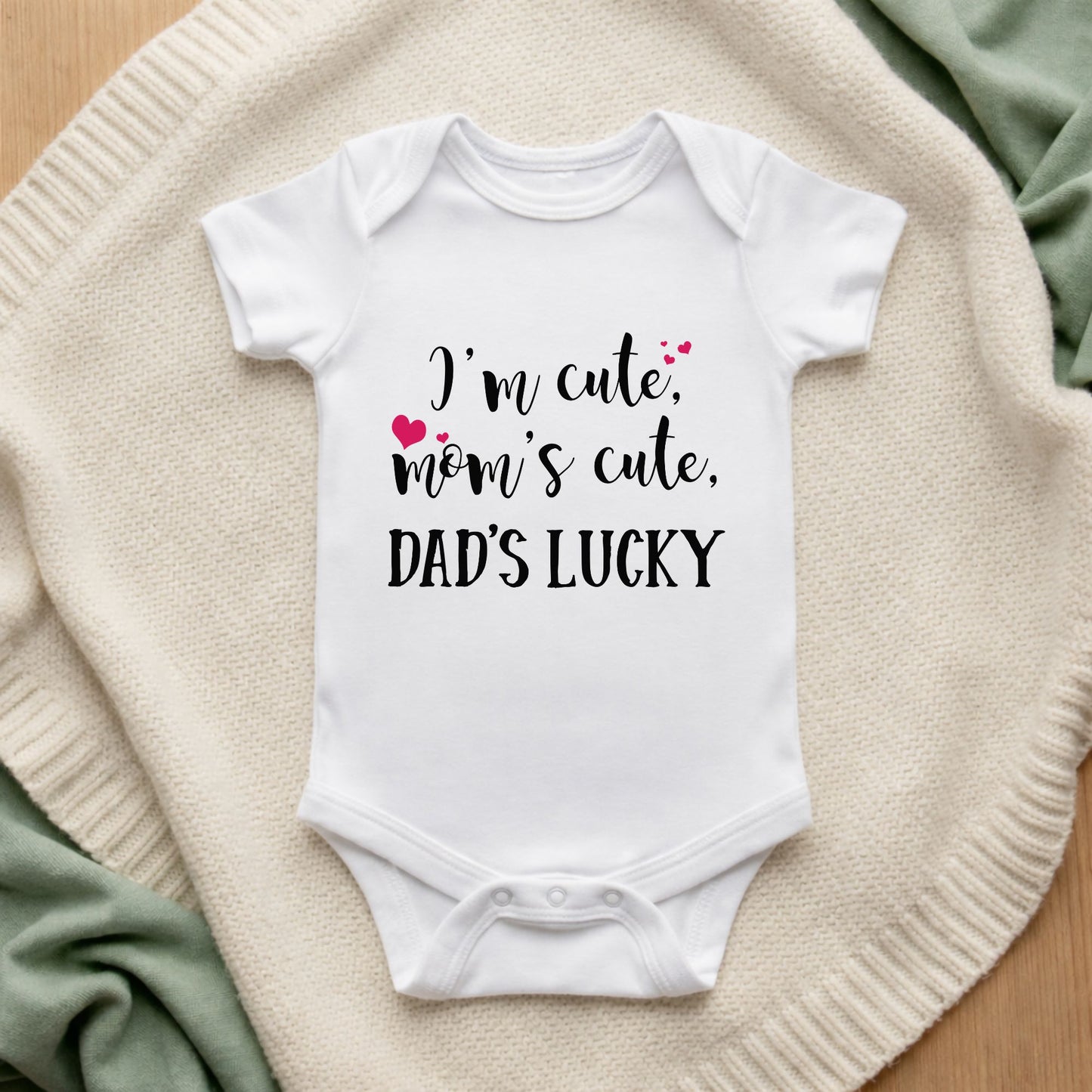 White baby onesie with text on a textured surface I'm Cute Mom's Cute Dad's Lucky Baby Vest