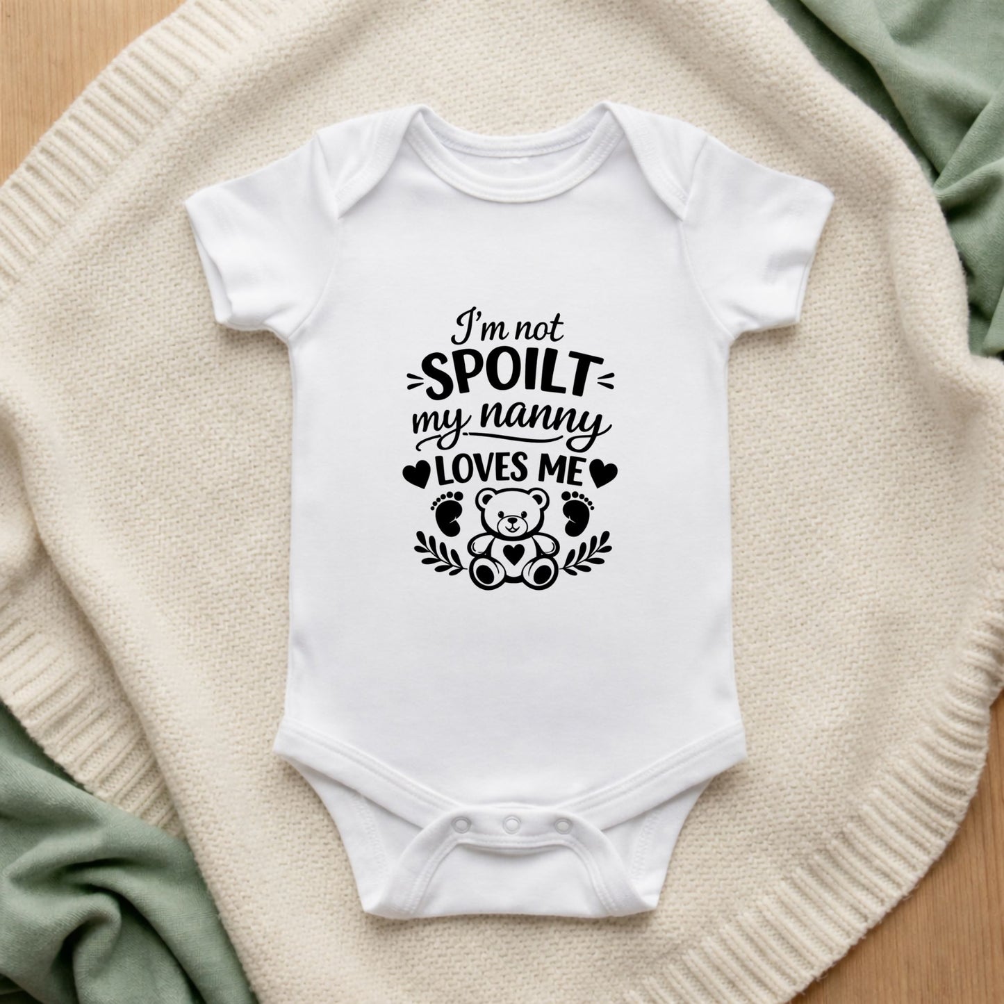 White baby onesie with text and a teddy bear graphic on a textured surface.