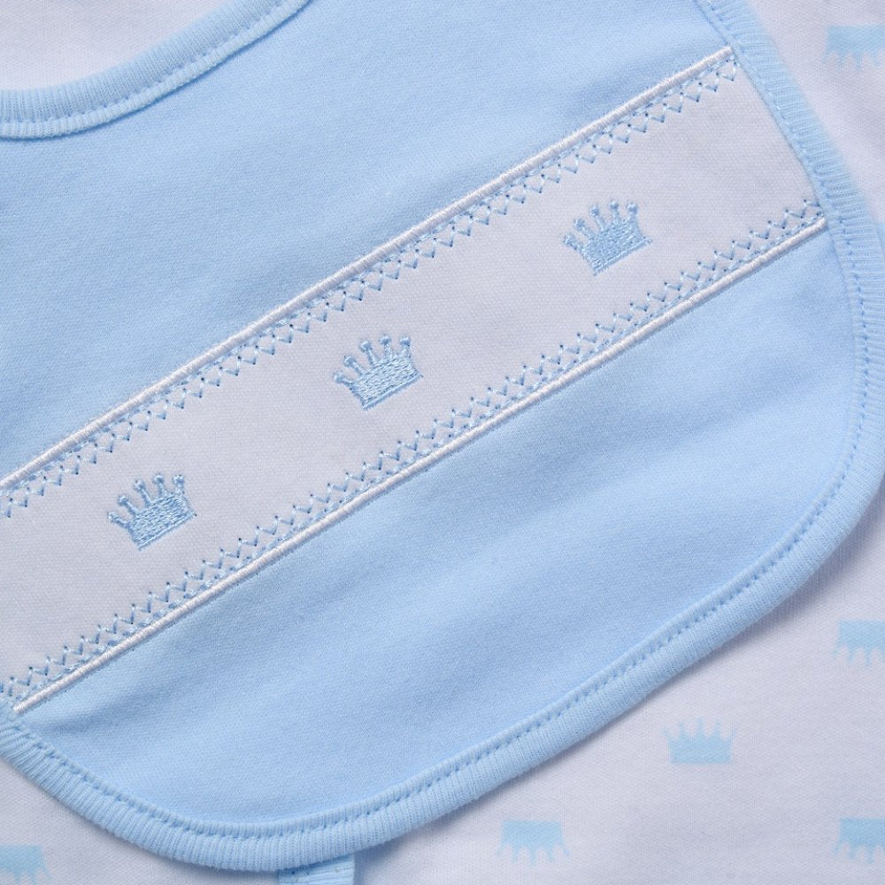 Close-up of a baby bib in light blue and white, featuring embroidered crown motifs and decorative stitching.