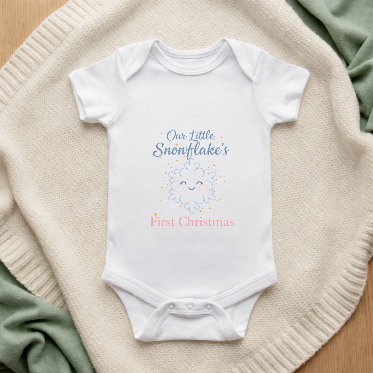 White baby onesie with 'Our Little Snowflake's First Christmas' text on a textured surface.