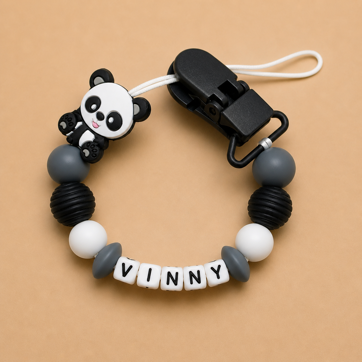 Pacifier clip with panda design and 'VINNY' letter beads on a beige background