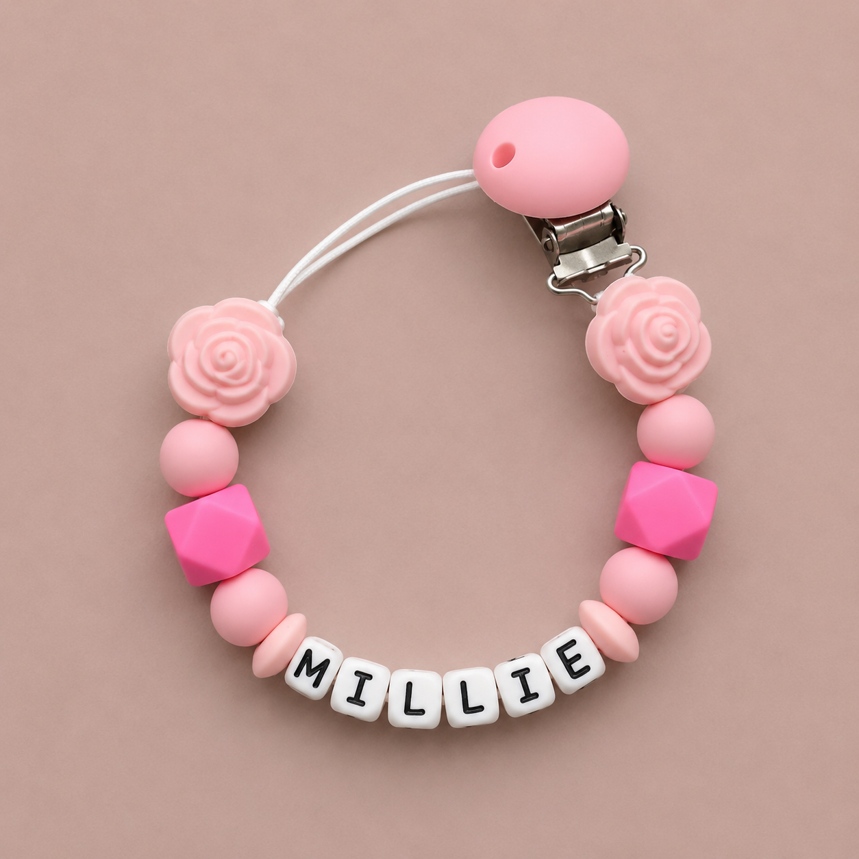 Pink and white pacifier clip with 'MILLIE' on a beige background