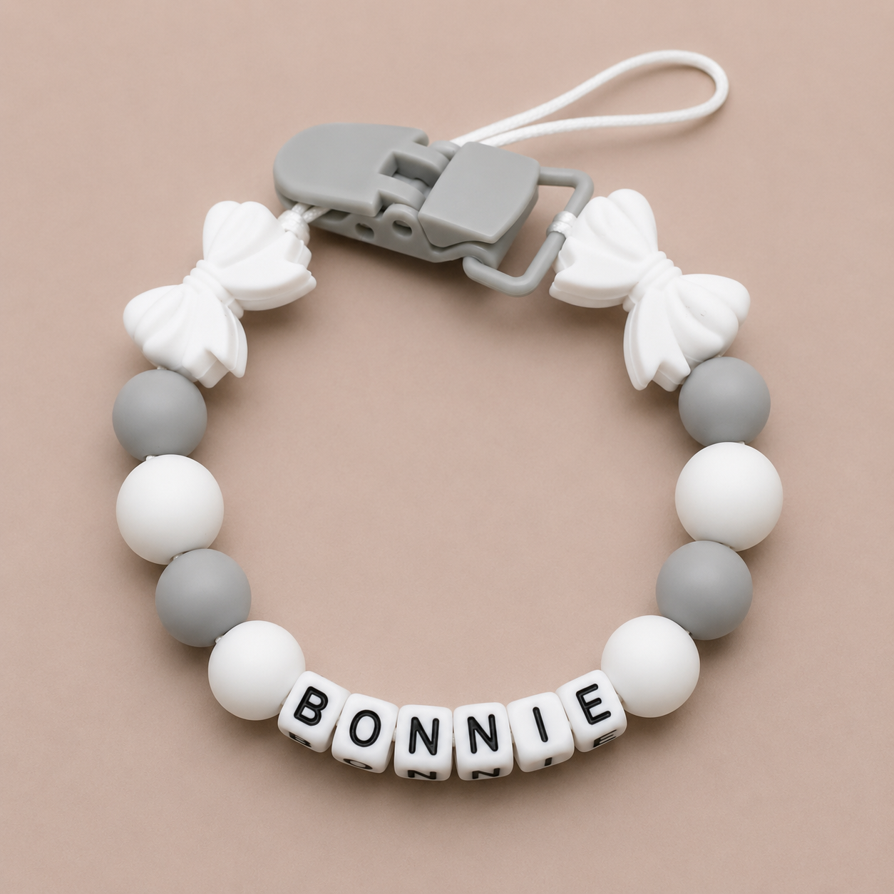 dummy clip with white and gray beads and 'BONNIE' letter beads on a beige background