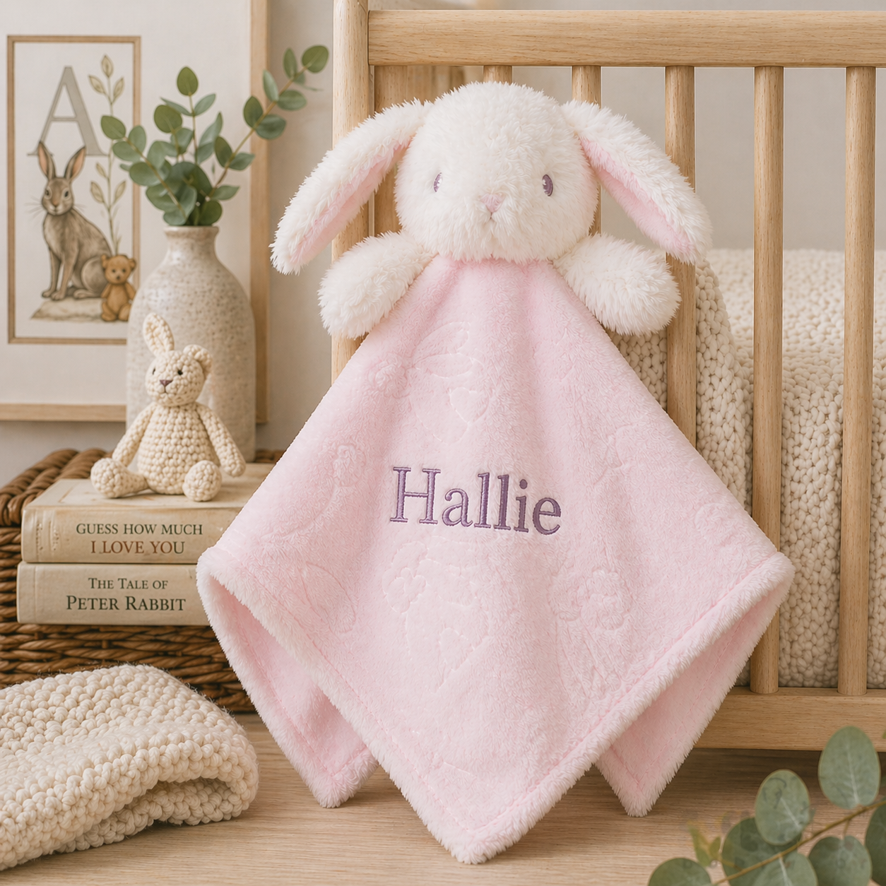 Pink bunny comfort blanket with 'Hallie' embroidered on it in a nursery setting.