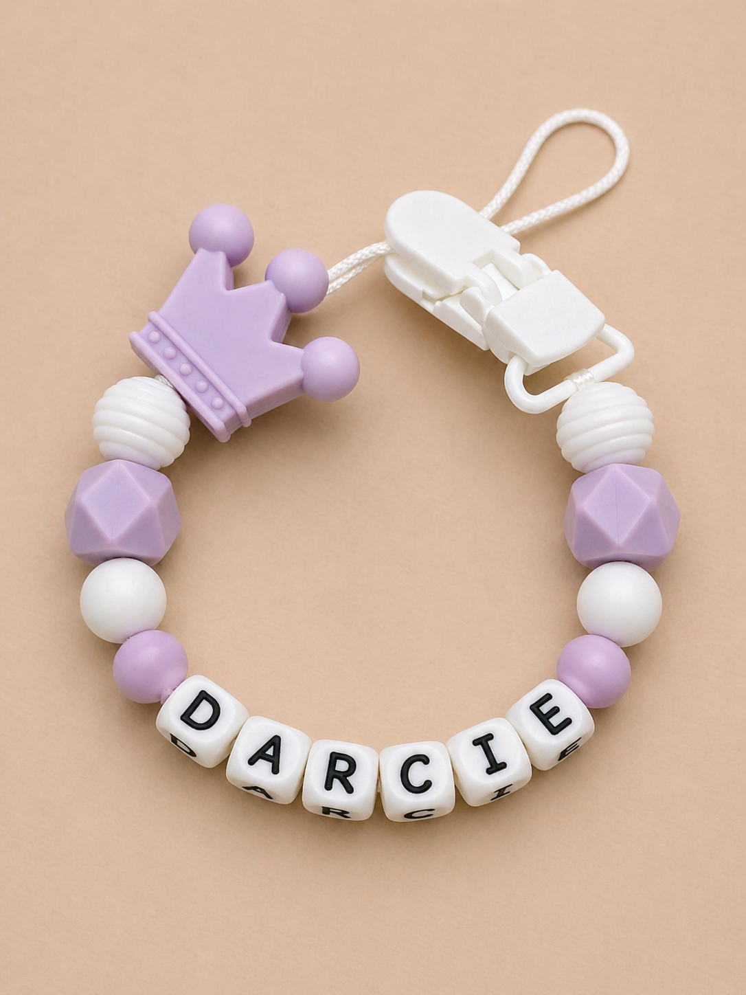 Baby teether with geometric beads and a crown-shaped clip on a beige background