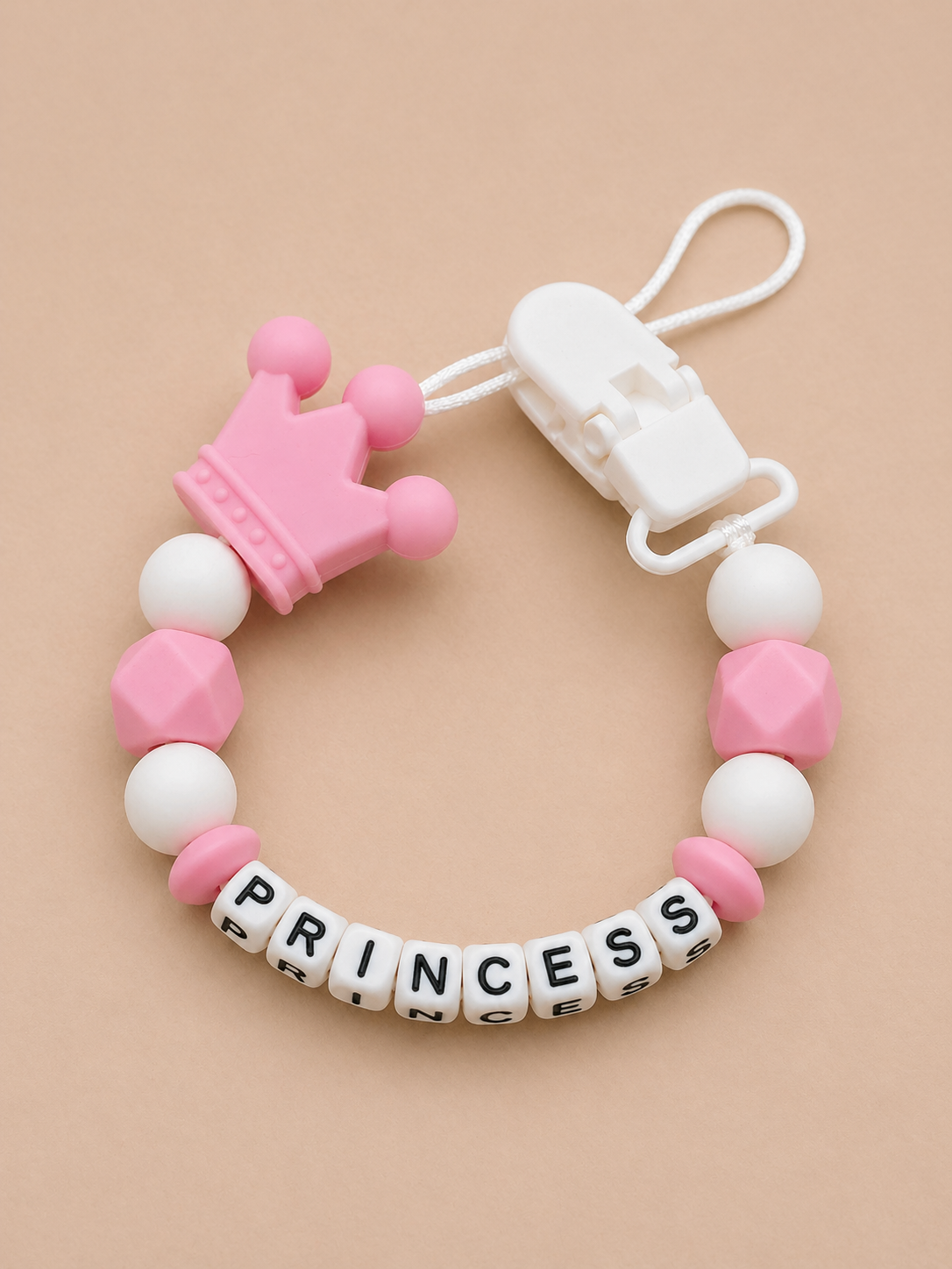 Baby teether with pink crown and 'PRINCESS' beads on a beige background