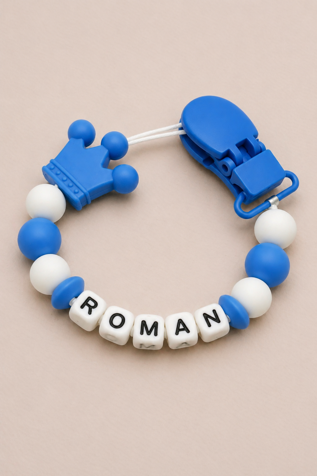 Blue and white teething ring with 'ROMAN' on a beige background
