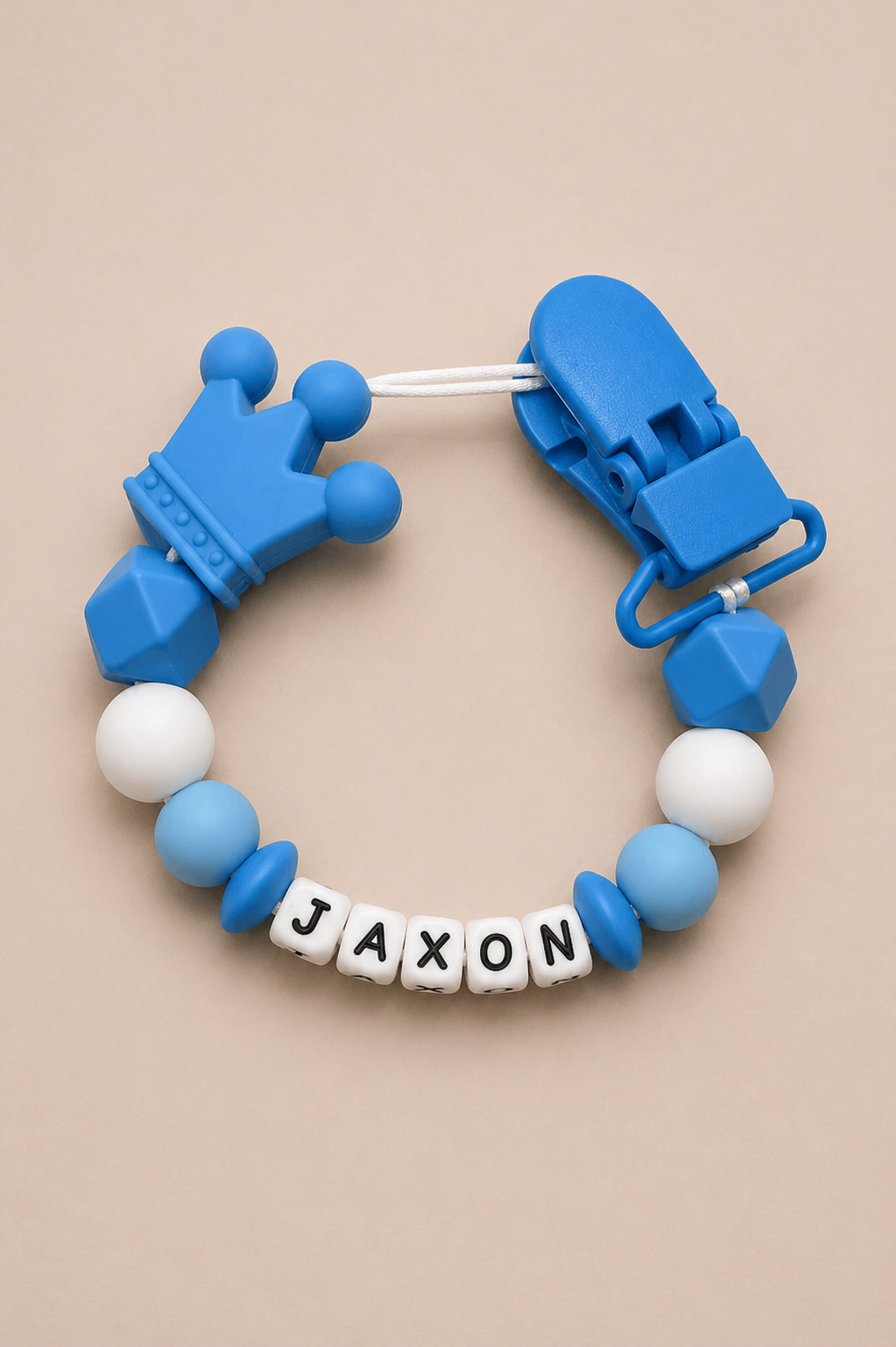 Blue and white teething ring with 'JAXON' name tag on a beige background