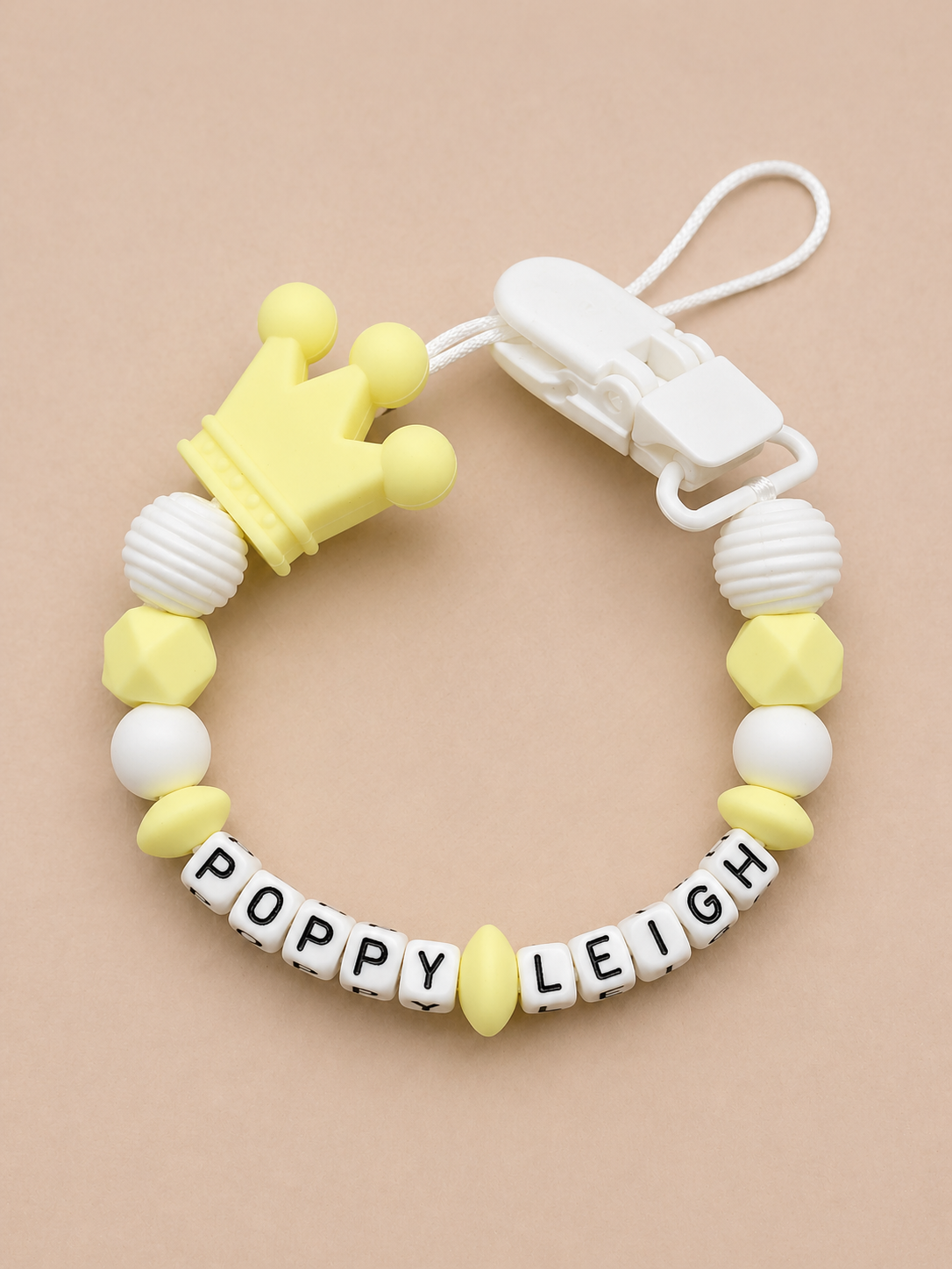 Baby teether with crown design and 'Poppy Leigh' beads on a beige background