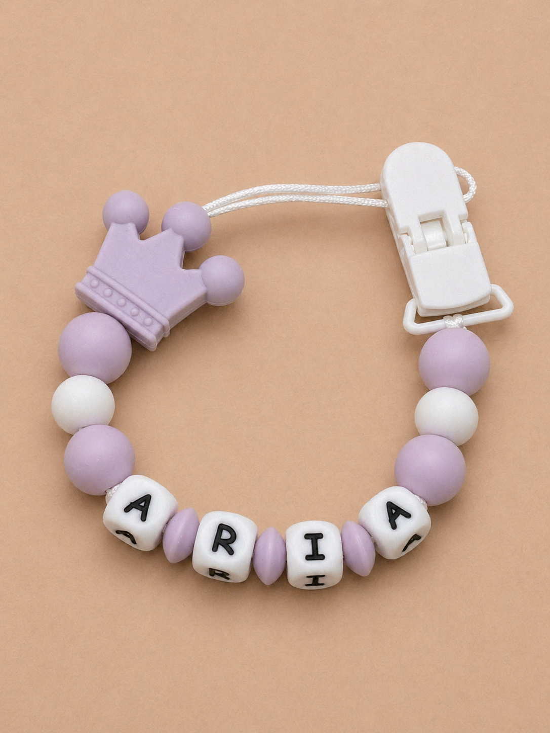 Silicone teether with purple and white beads and a crown charm on a beige background