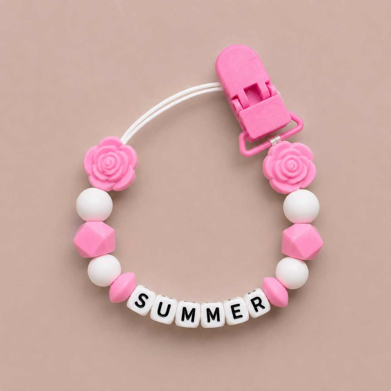 Pink and white dummy clip with 'SUMMER' letters on a beige background