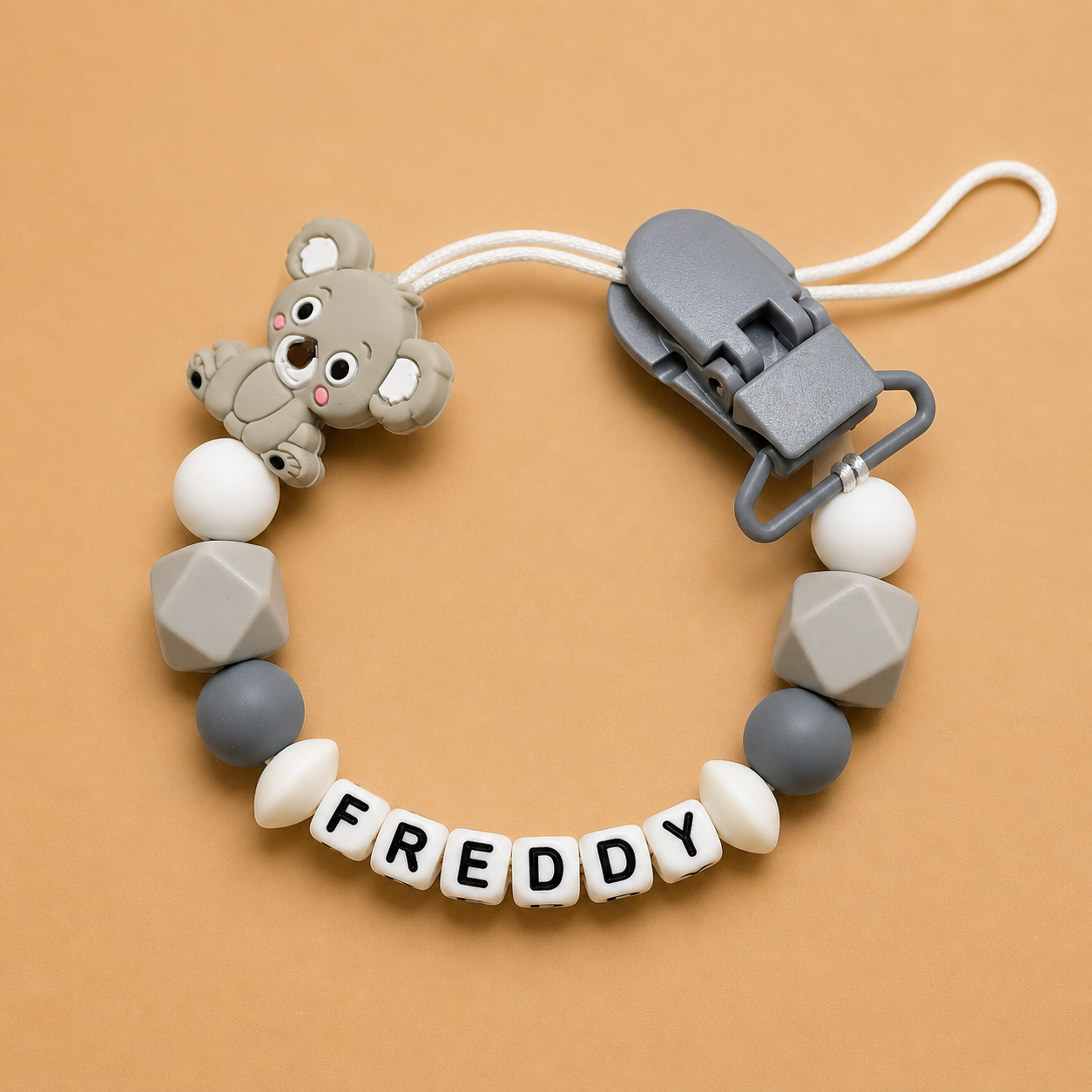 dummy clip with bear-shaped clip and 'FREDDY' beads on a beige background