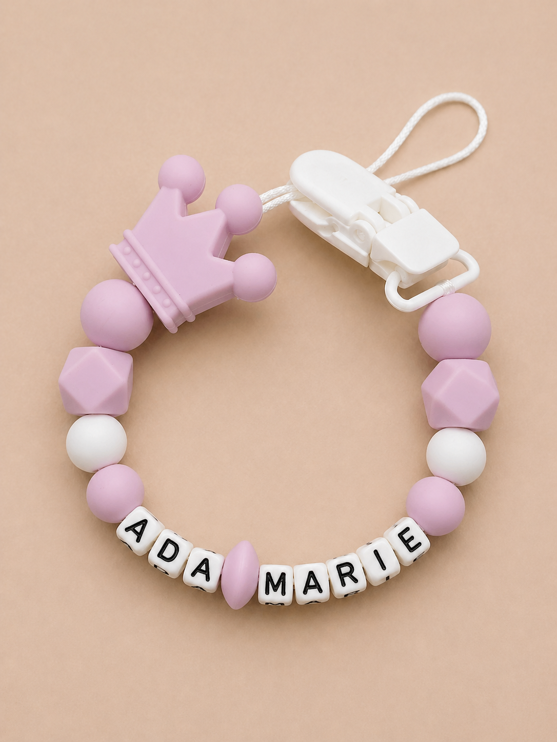 Pink and white teething ring with name beads on a beige background