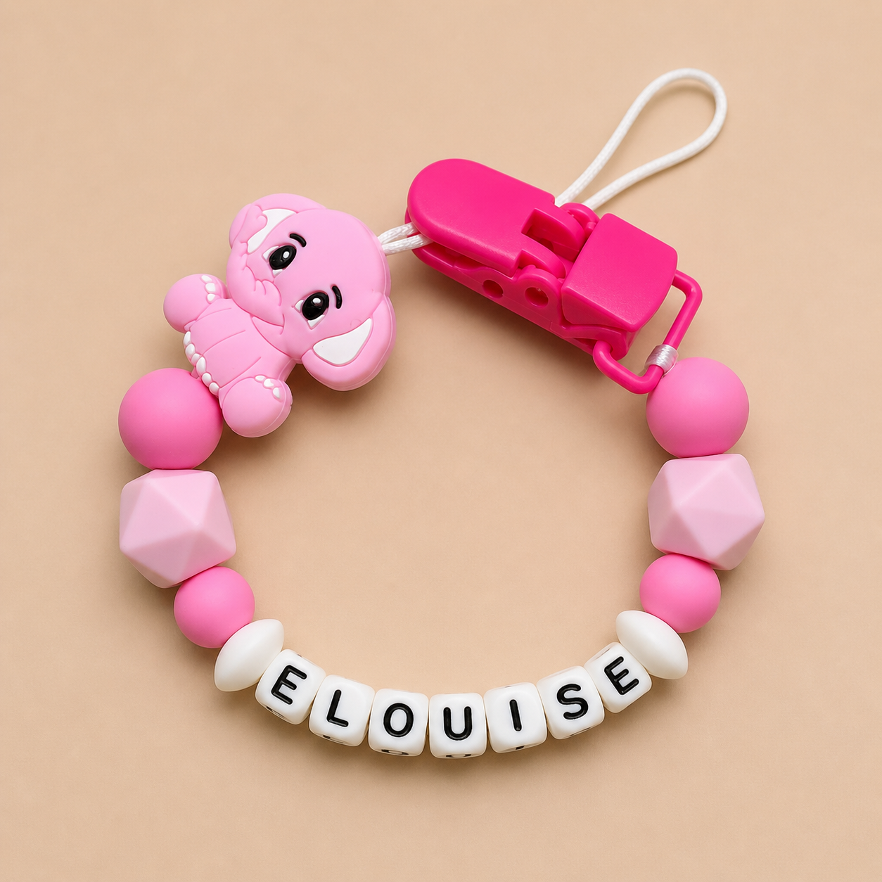 Pink dummy clip with a clip and 'ELOUISE' name on a beige background