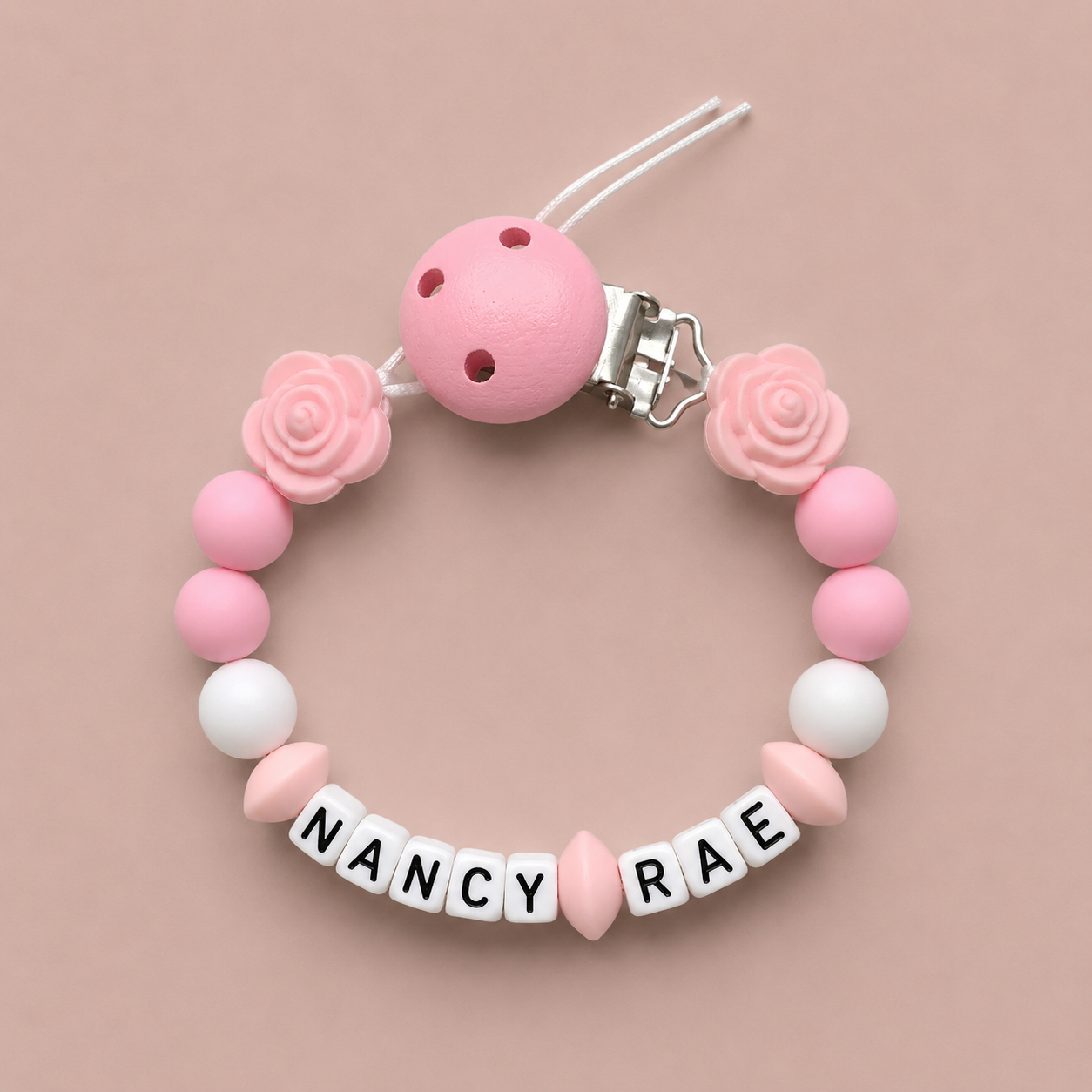 Pink and white baby dummy clip with 'Nancy Rae' on a beige background