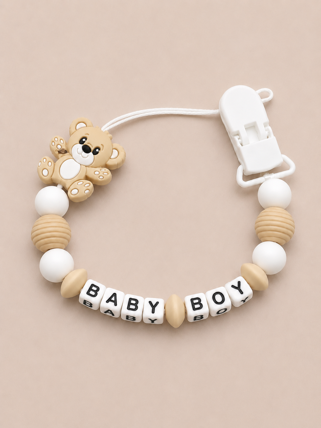 Baby dummy clip with teddy bear design and 'BABY BOY' beads on a beige background
