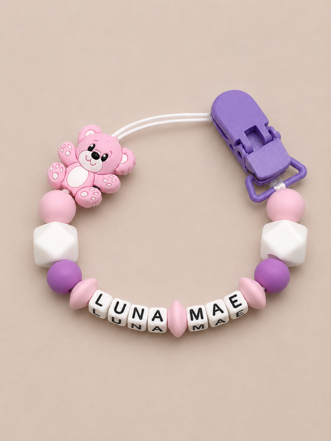 Baby dummy clip with colorful beads and a bear-shaped charm on a beige background