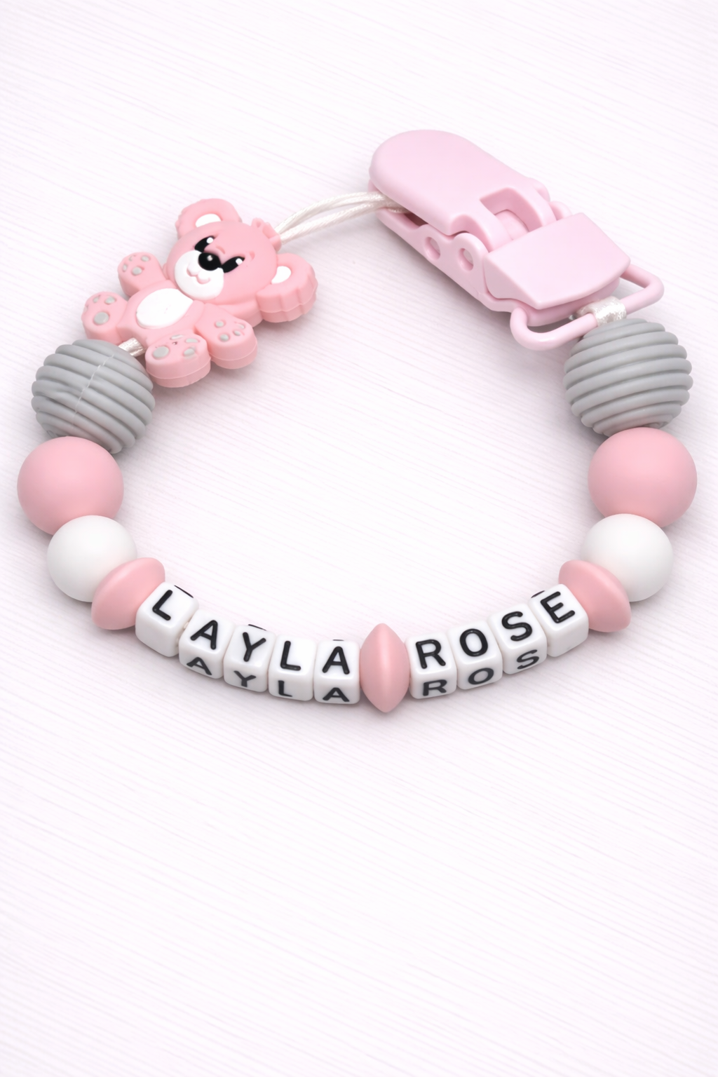 Baby teething bracelet with pink and gray beads and a bear charm on a white background