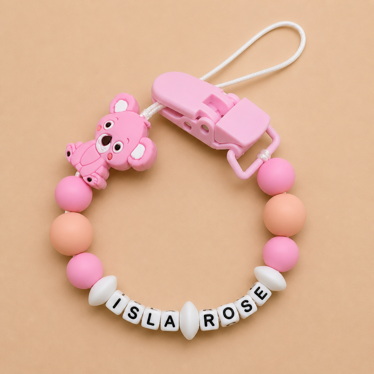 Pink baby dummy clip with bear design and 'ISLA ROSE' beads on a beige background