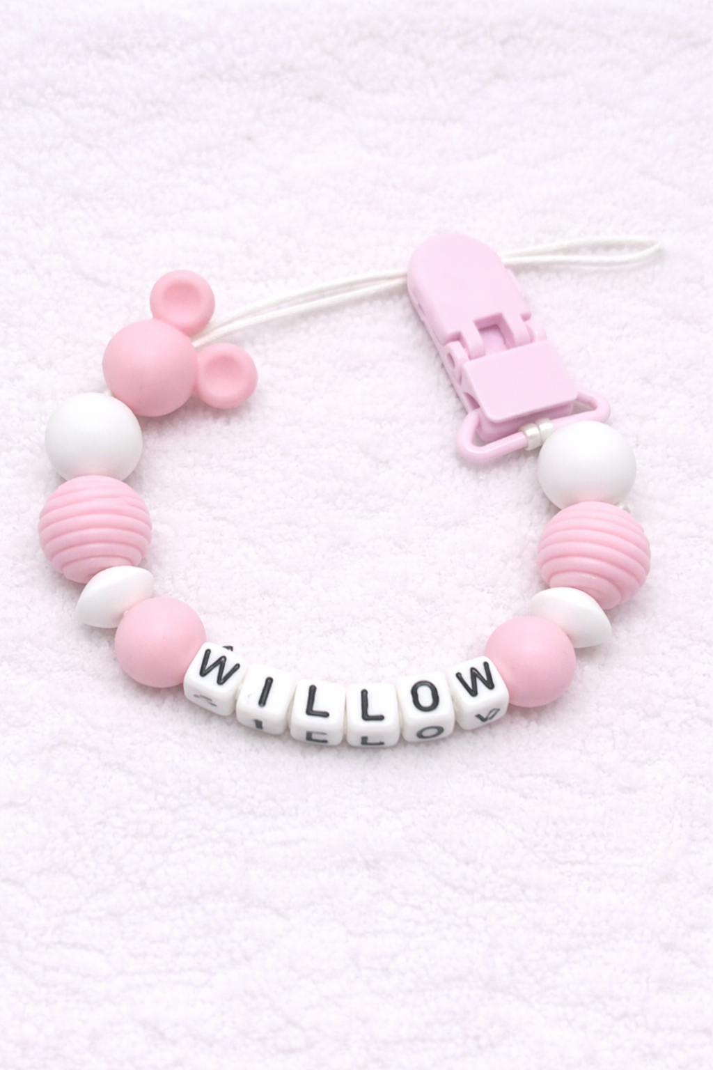 Pink and white dummy clip with letter beads on a light pink background