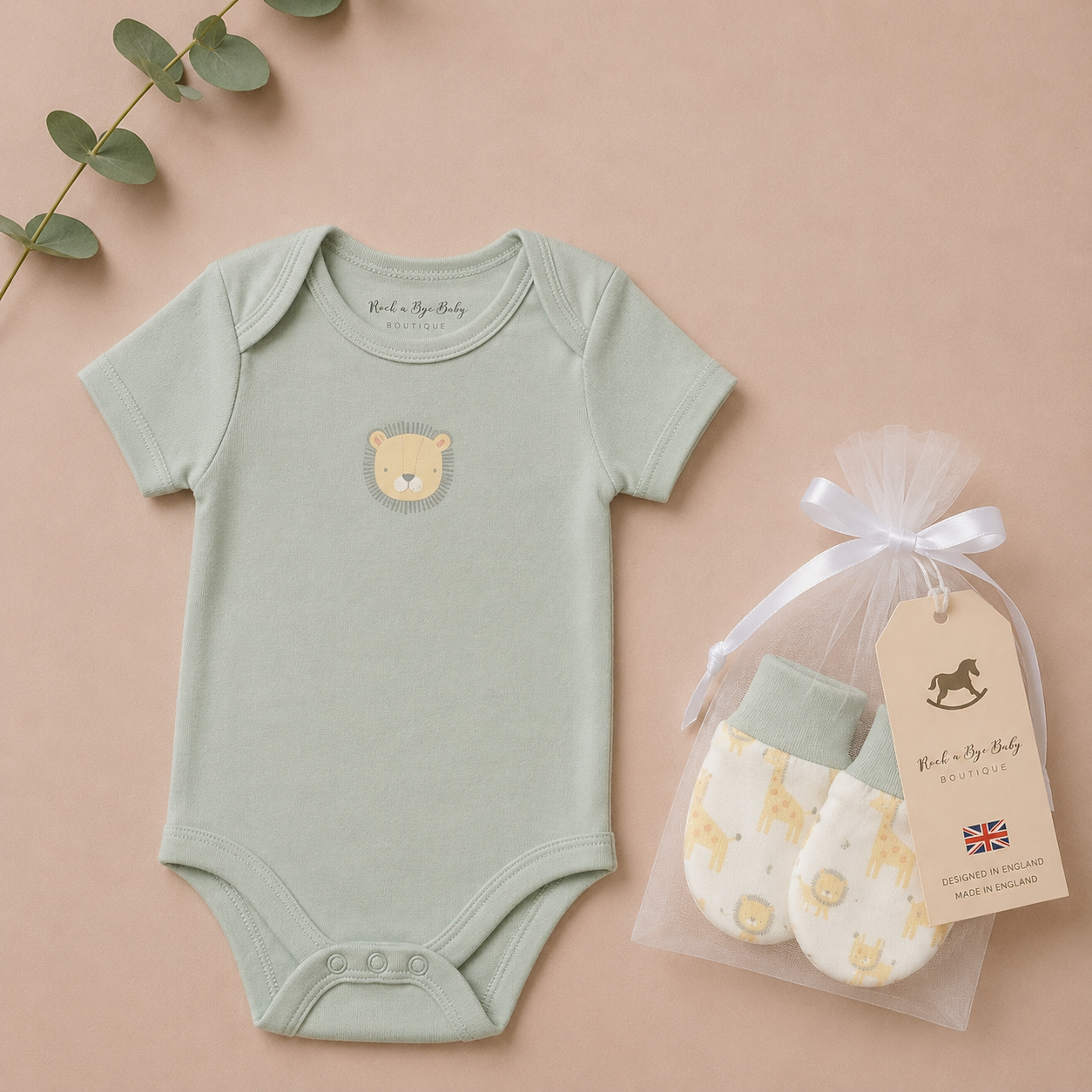 Green baby onesie with bear design and white mittens in clear bag on beige background