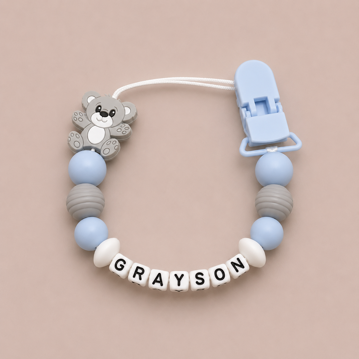 dummy clip with bear charm and 'GRAYSON' name on a beige background