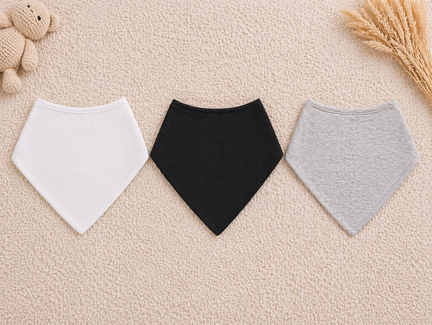 Three baby bibs in white, black, and gray on a beige surface.