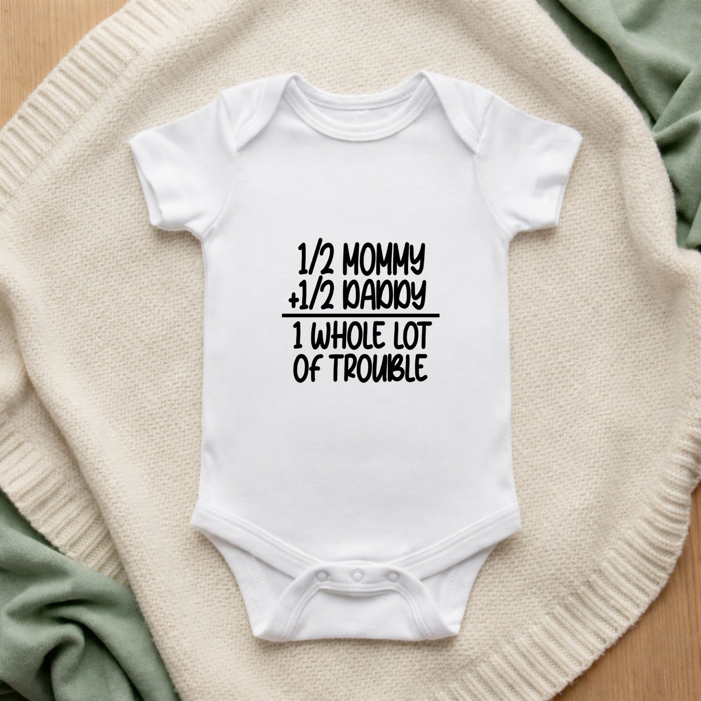 White baby onesie with text on a textured surface 1/2 Mommy + 1/2 Daddy = 1 Whole Lot of Trouble Baby Vest
