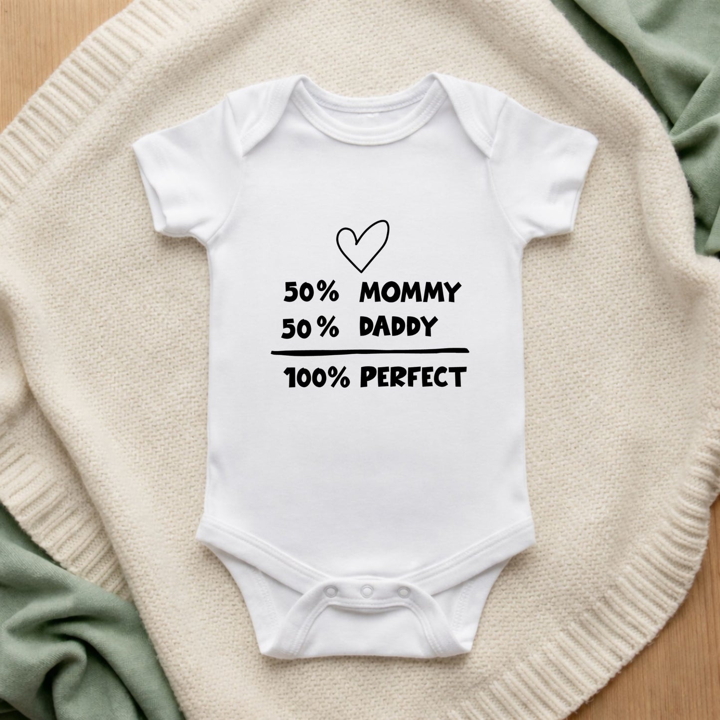 White baby onesie with text on a textured surface 50% Mommy 50% Daddy 100% Perfect Baby Vest