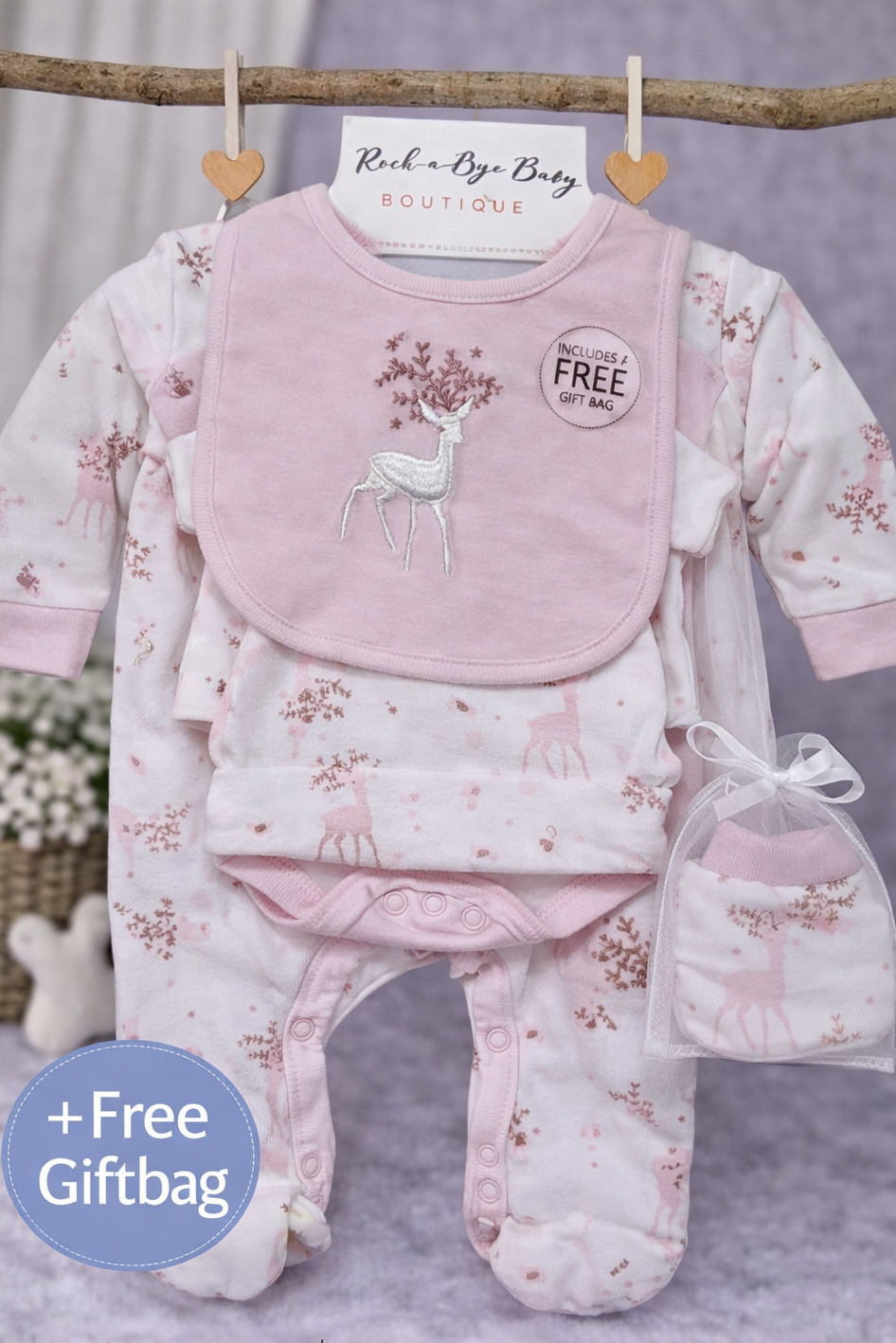 Baby gift set with pink deer-themed outfit, bib, and booties on a gray background.