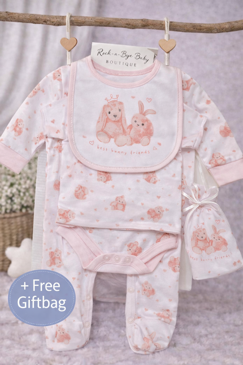 Baby girl gift set with pink and white design, including a bib and footed romper, on a branch with a free giftbag offer.