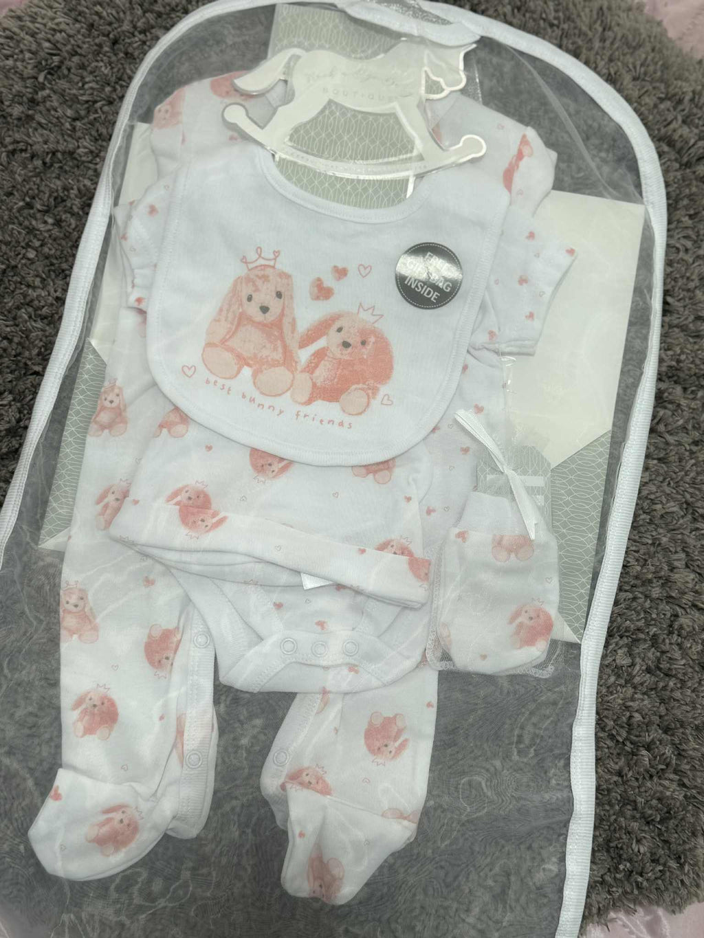 Baby clothing set with bib, pants, and booties in a clear bag on a textured surface.
