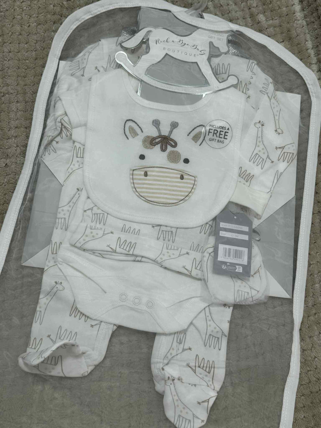 Baby romper with bib and booties set in clear packaging on a textured surface