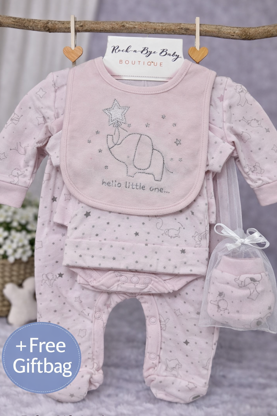 Baby gift set with pink outfit, bib, and booties hanging on a branch with a 'Rock a Bye Baby' sign.