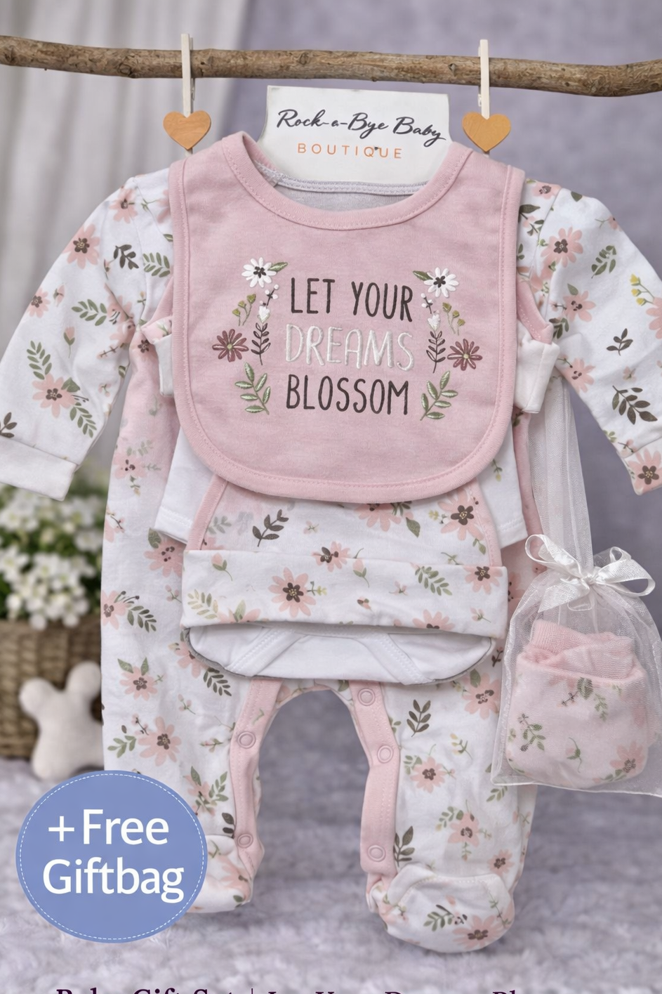 Baby gift set with bib, onesie, and pants featuring floral patterns and text, hanging on a branch.