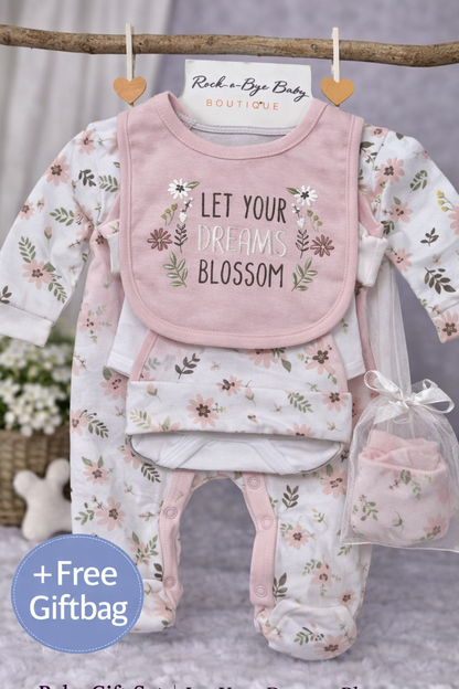 Baby gift set with bib, onesie, and pants featuring floral patterns and text, hanging on a branch.