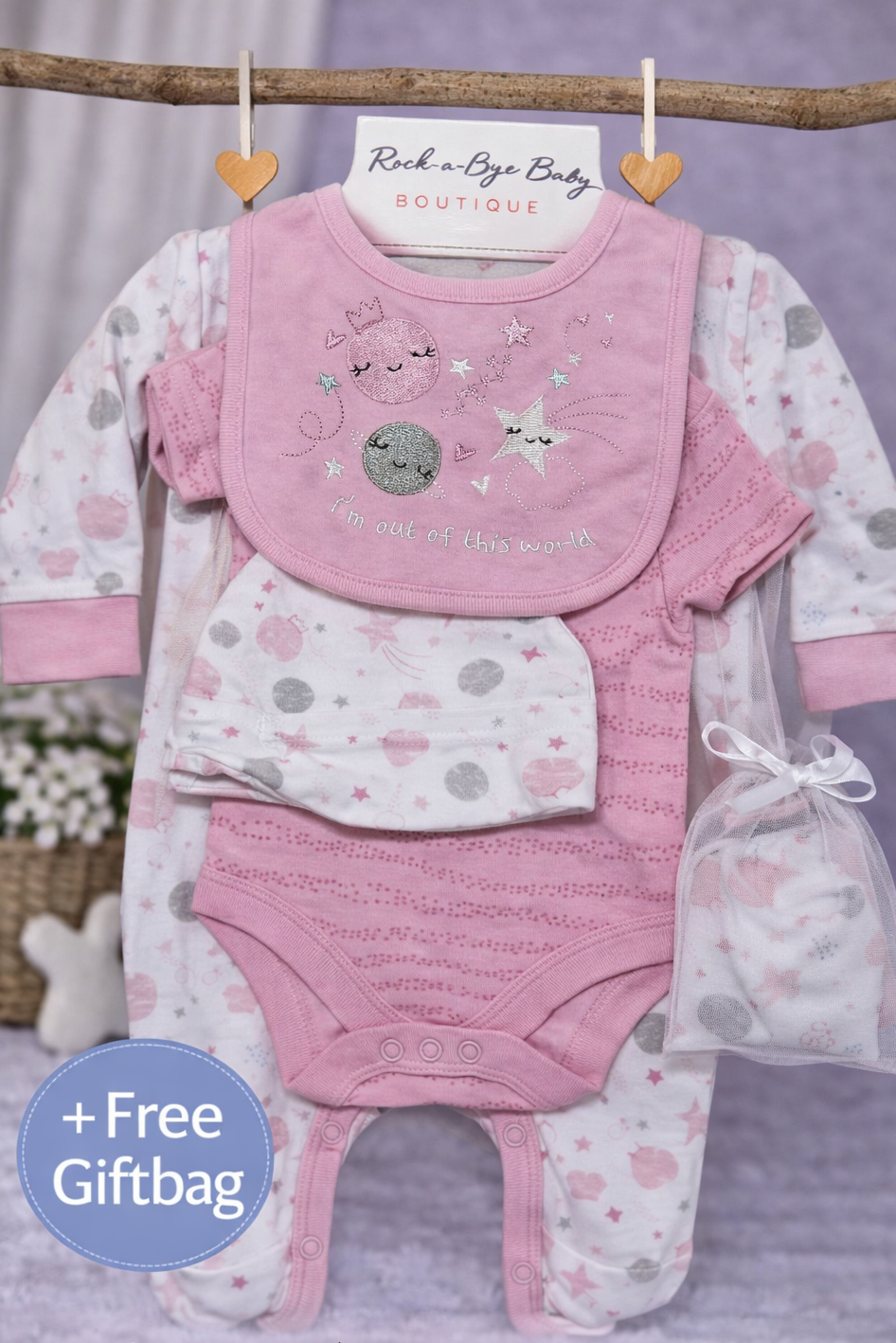 Baby gift set with pink bib, shirt, pants, and free giftbag on a wooden stick against a purple background.
