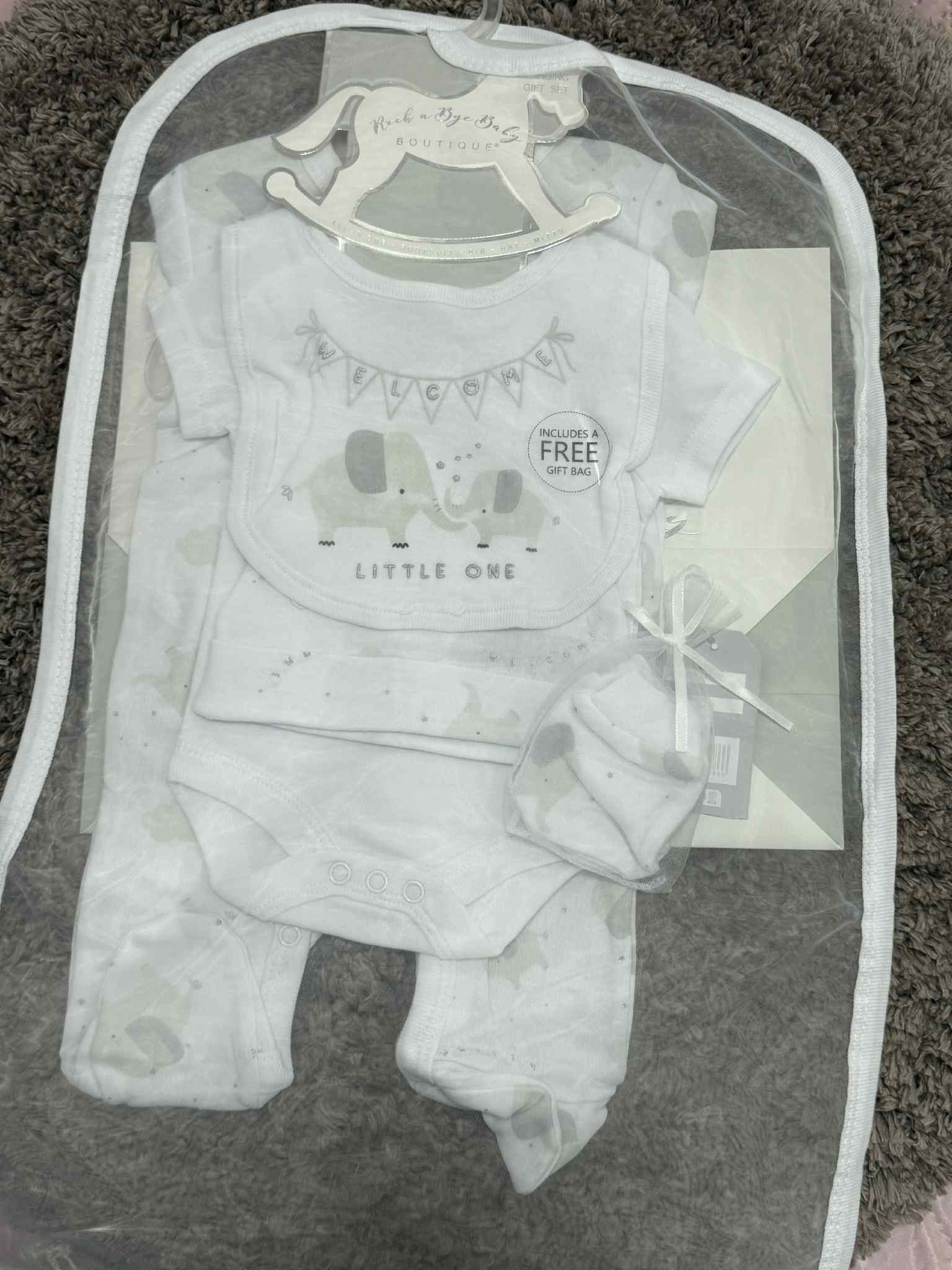 Baby outfit set with onesie, pants, and bib in a clear bag on a carpeted floor.