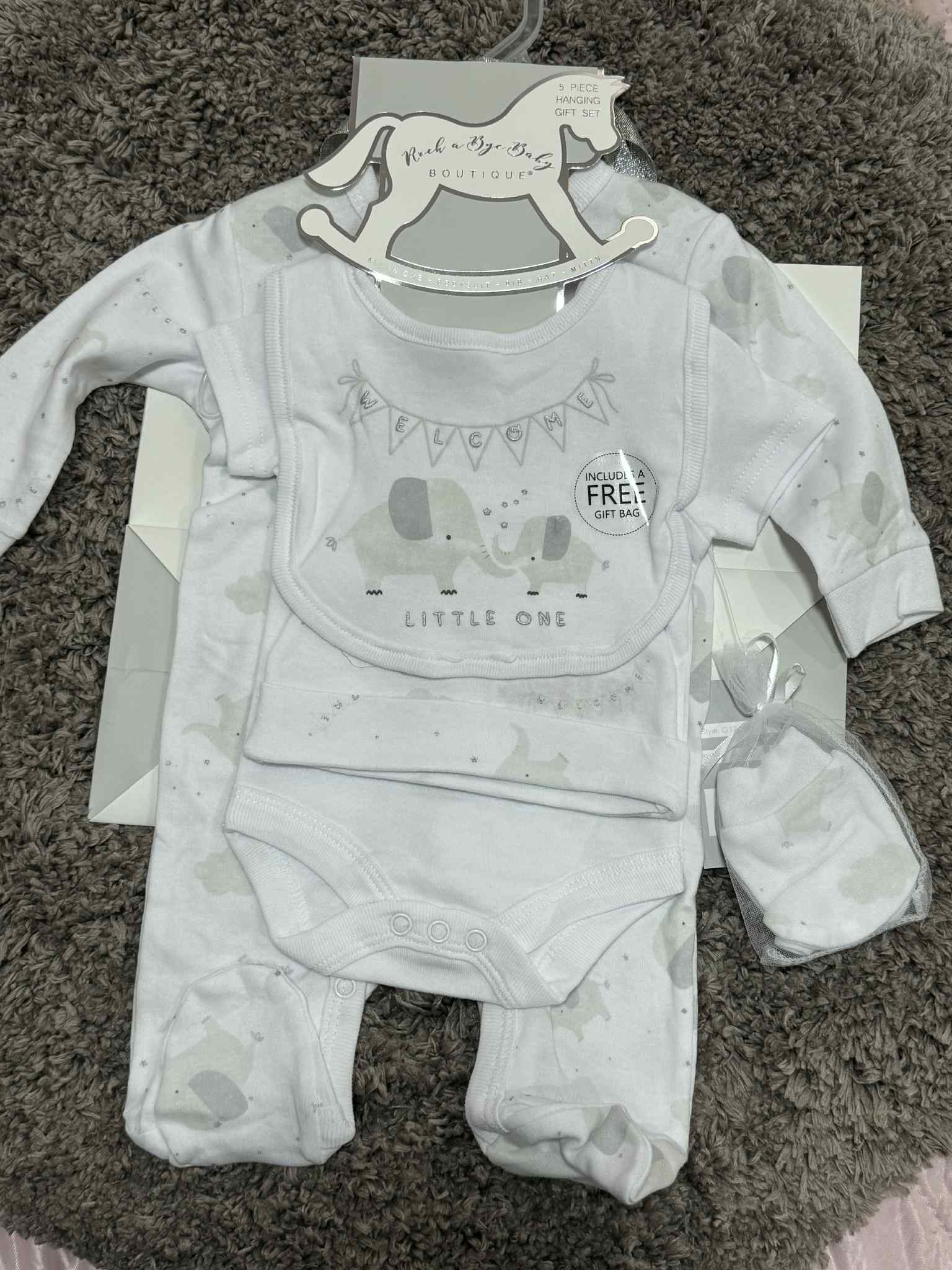 Baby outfit set with onesie, bib, and booties on a hanger with tags.