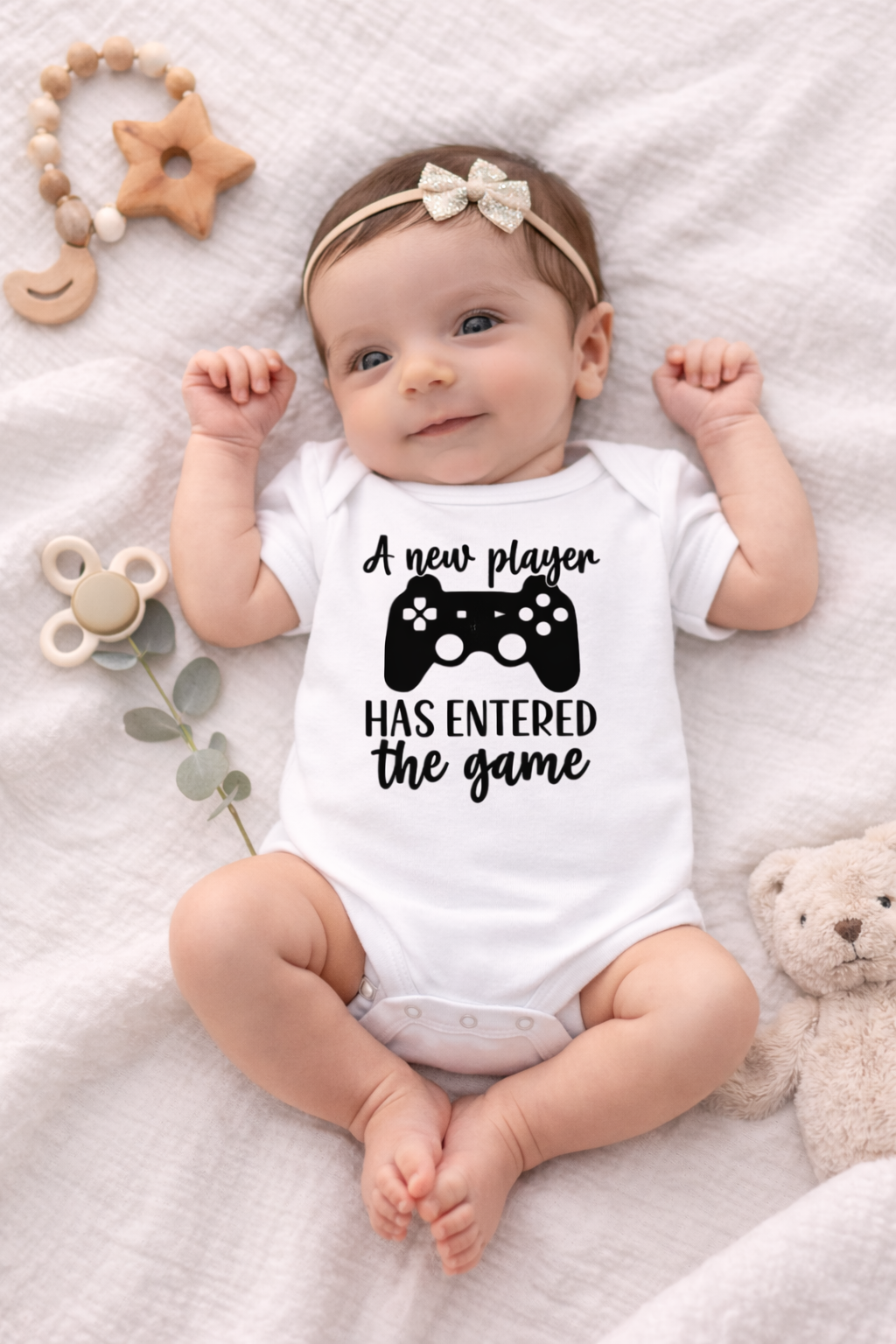 Baby wearing a onesie with text and a game controller graphic on a soft surface.