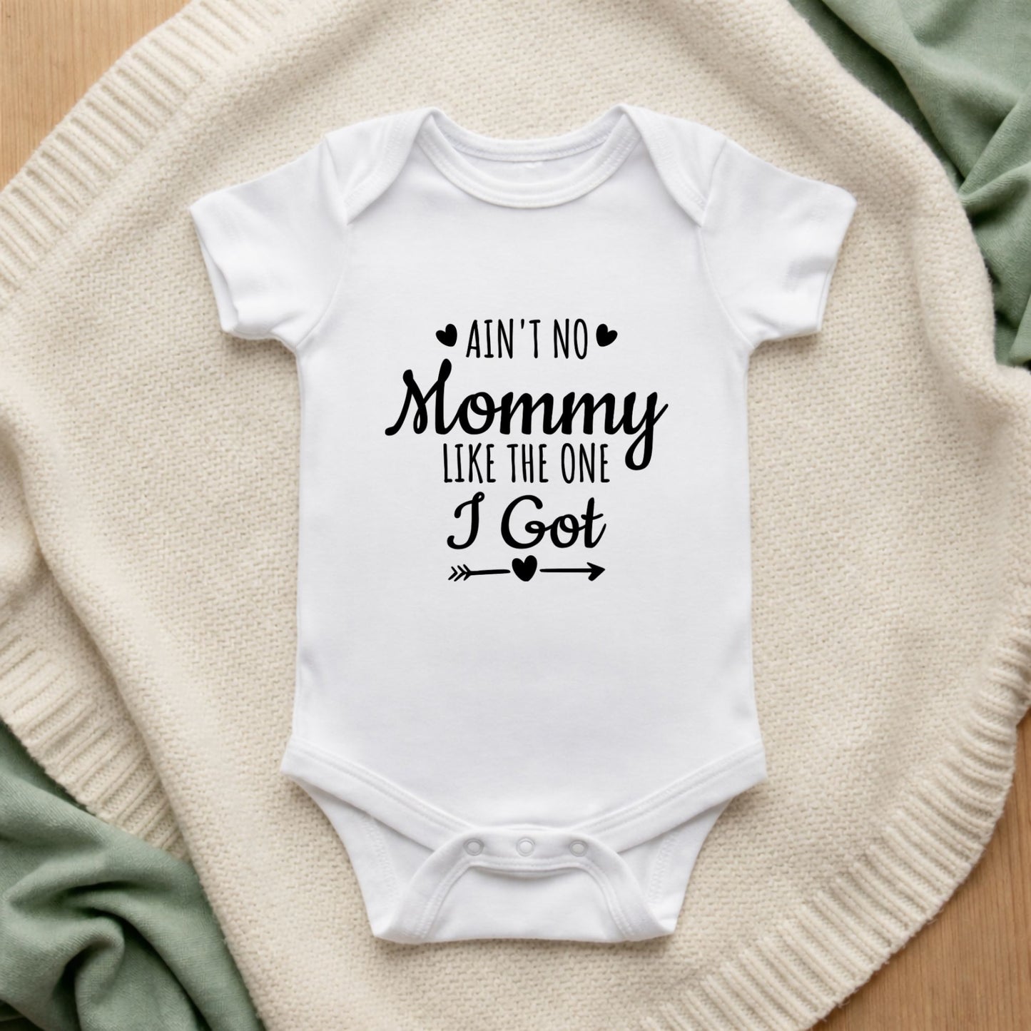 White baby onesie with text on a textured surface Ain't No Mommy Like the One I Got Baby Vest