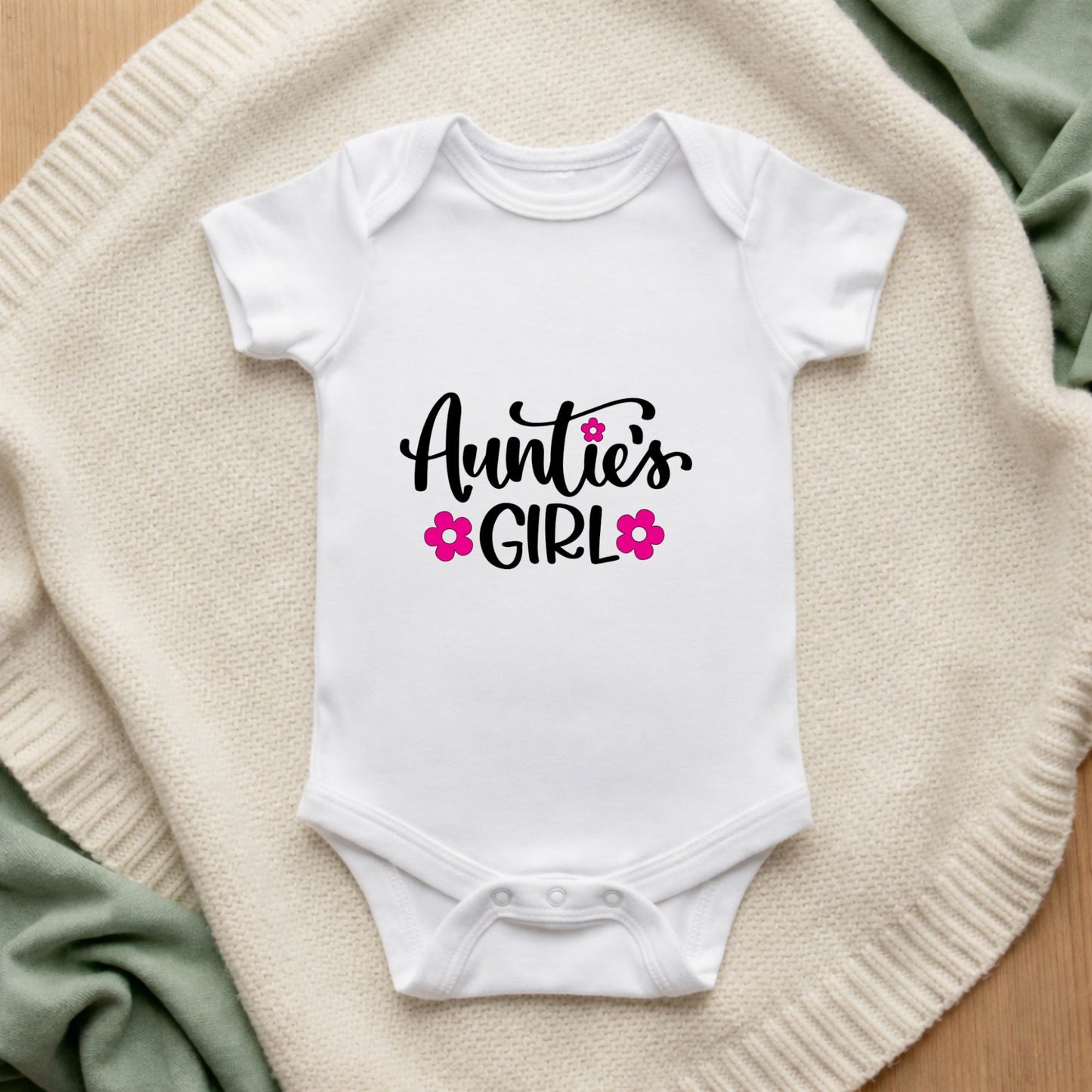 White baby onesie with 'Auntie's Girl' text on a textured surface Auntie's Girl Baby Vest
