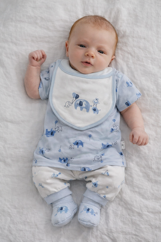Baby wearing a blue outfit with elephant patterns on a white blanket