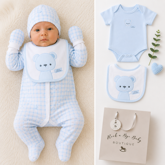 A baby sleep suit set shown on a baby doll and as a flat lay, featuring a light blue and white gingham check footed sleeper with matching hat and mittens, a white bib with a light blue bear graphic, and a gift bag from 'Rock a Bye Baby Boutique'.
